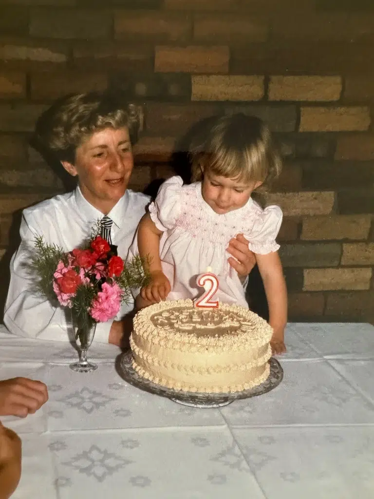 Toddler Nicole with her mum, about to blow out the candle on a walnut custard cake