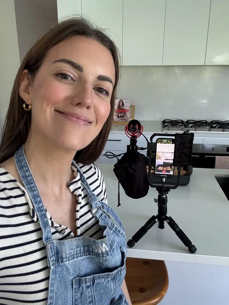 Nicole Maguire in an apron filming a dinner recipe on a phone in her kitchen