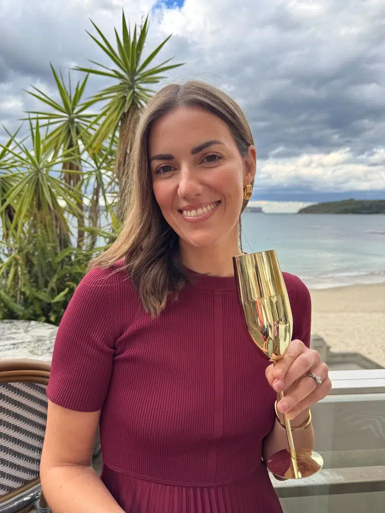 Nicole Maguire smiling beside the beach holding a gold glass