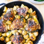 Top view chicken in baking dish with side of greens and lemon