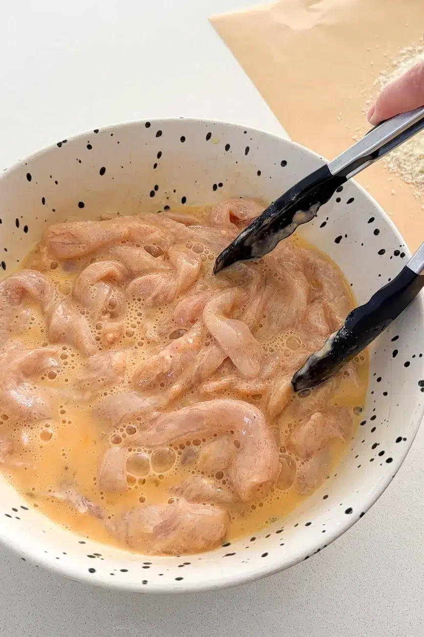 chicken fingers tossed through egg using tongs