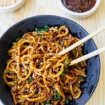 close up dan dan noodles in bowl with chopsticks