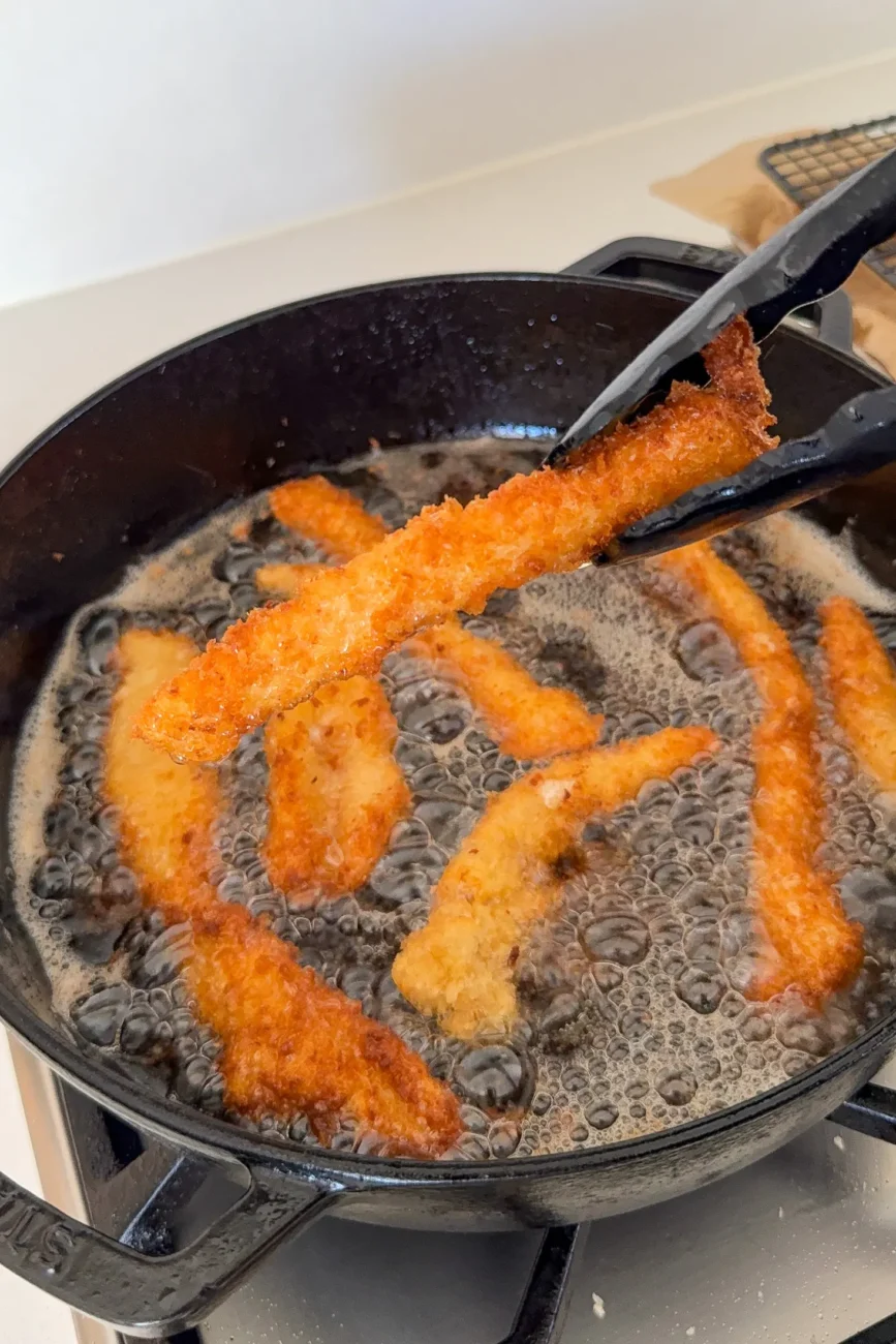 cooked crispy chicken finger held with tongs