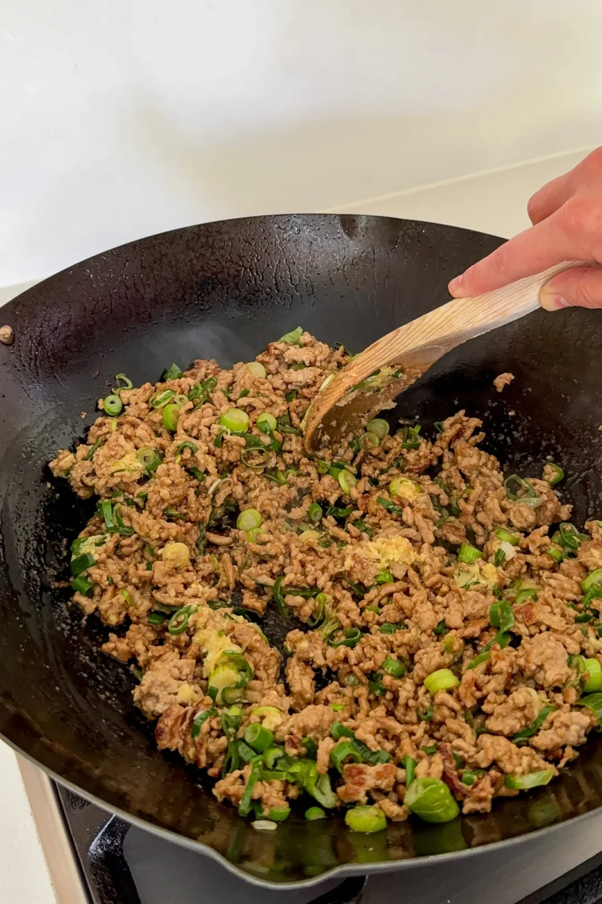 ginger garlic and spring onions being stirred through pork