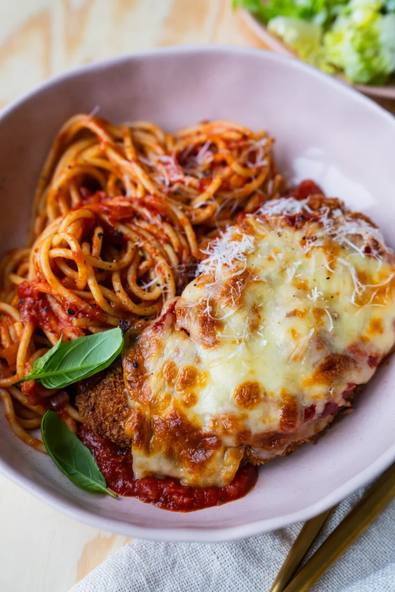 Chicken parmigiana plated with spaghetti and a side of salad