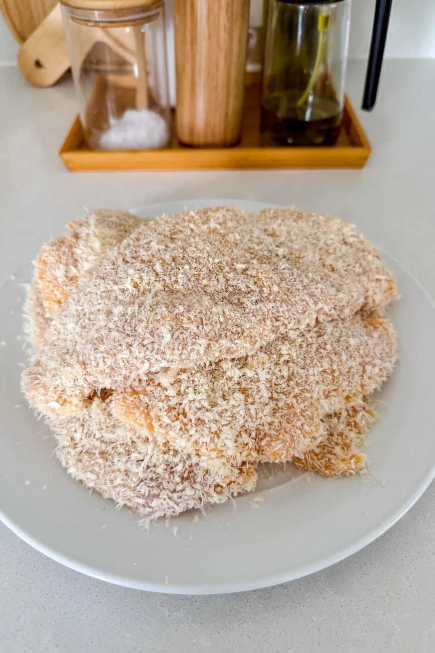 Crumbed chicken schnitzels stacked on plate ready for frying