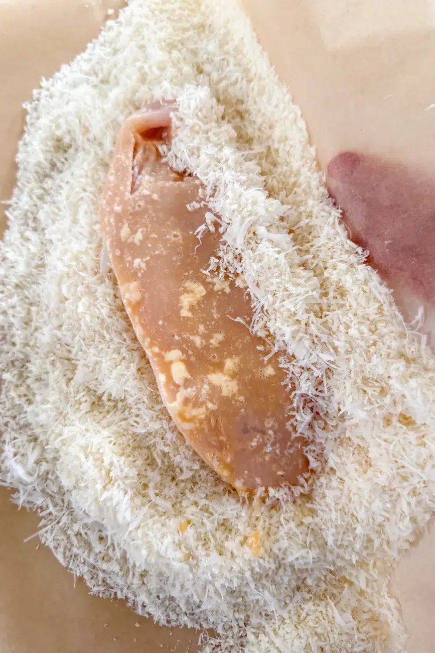 Egg coated chicken being pressed into parmesan panko breadcrumbs using baking paper